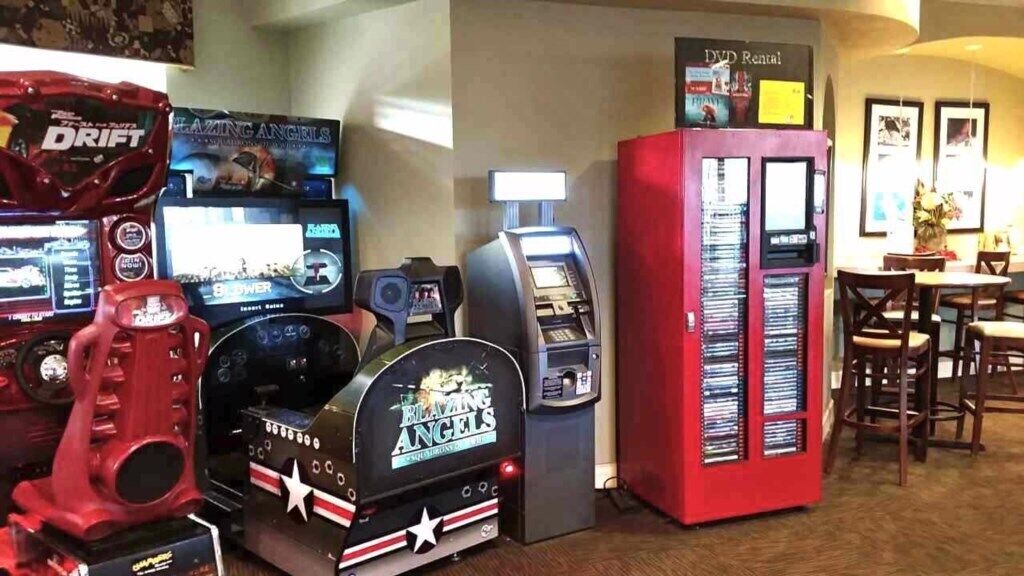 A row of gaming machines, a DVD rental kiosk, and a DVD rental machine.