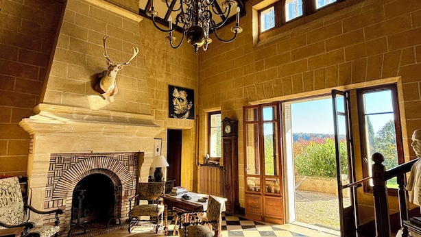 Una habitación amplia con suelo a cuadros, chimenea, candelabro y un ventanal con vistas.