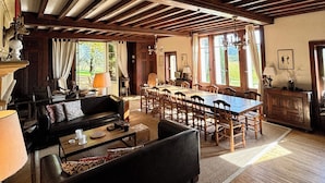 Un cuarto espacioso con una gran mesa de comedor, vigas de madera en el techo y una zona de estar acogedora con un sofá y sillones.