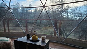 Habitació acollidora amb una finestra gran, una maleta rústica, una tetera i una tassa sobre un estotge.