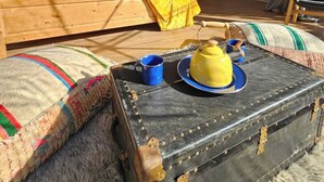 Un allotjament en una tenda acollidora, amb un llit de fusta, una taula petita amb una tetera i una tassa, i una zona de seients confortable.