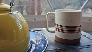 Un ralador groc sobre un safata blau, una tassa blanca amb el text 'PENDLETON' i una vista d'arbres a través d'una finestra.