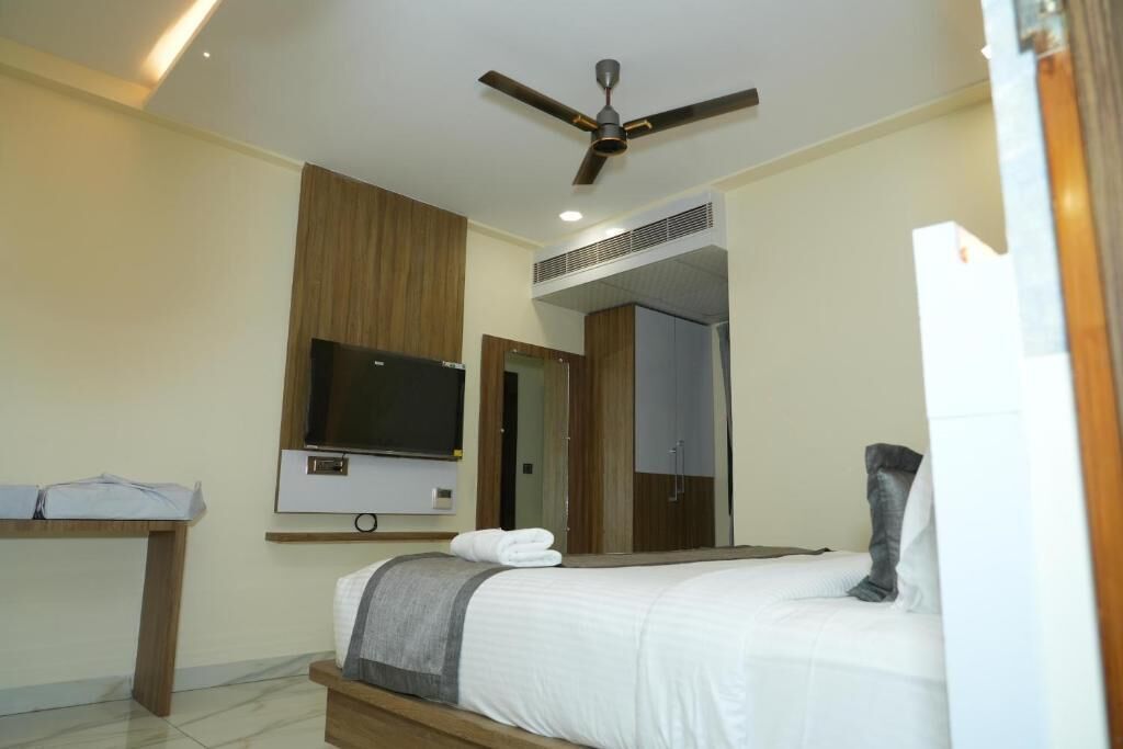 A modern hotel room with a bed, a flat-screen TV, a ceiling fan, and a wooden desk.