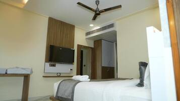 A modern hotel room with a bed, a flat-screen TV, a ceiling fan, and a wooden desk.