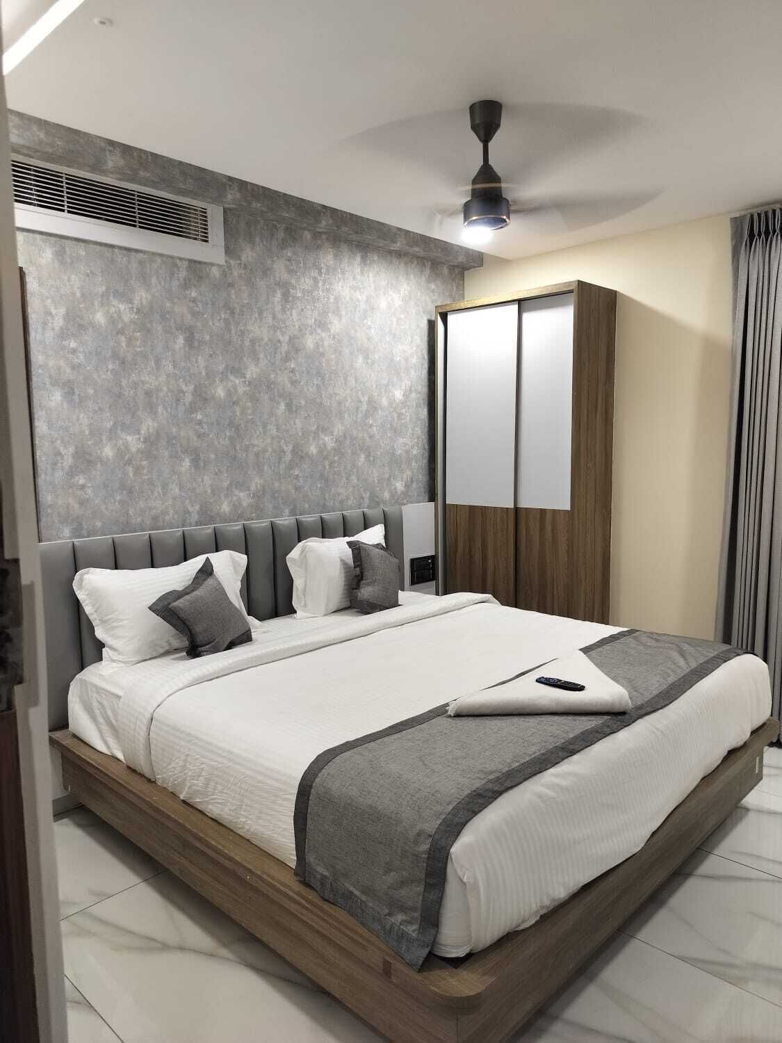 A modern hotel room with a large bed, a ceiling fan, a wardrobe, and a window with curtains.