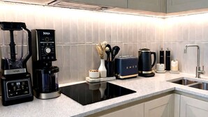 A modern kitchen with a built-in induction cooktop, a coffee maker, a toaster, and a kettle. - Stylish 2-bed Apartment With Patio in Chiswick (London)