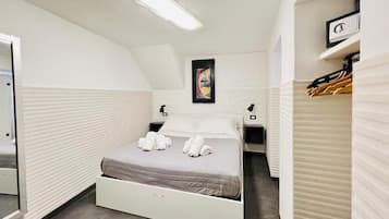 Habitación de hotel con cama, mesita de noche, espejo, un cuadro colgado en la pared y perchero.