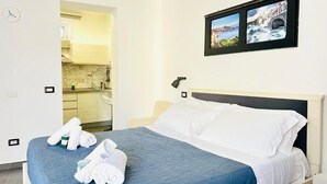 Ein Hotelzimmer mit Bett, Nachttisch, Wandfernseher und Blick auf die Küche.
