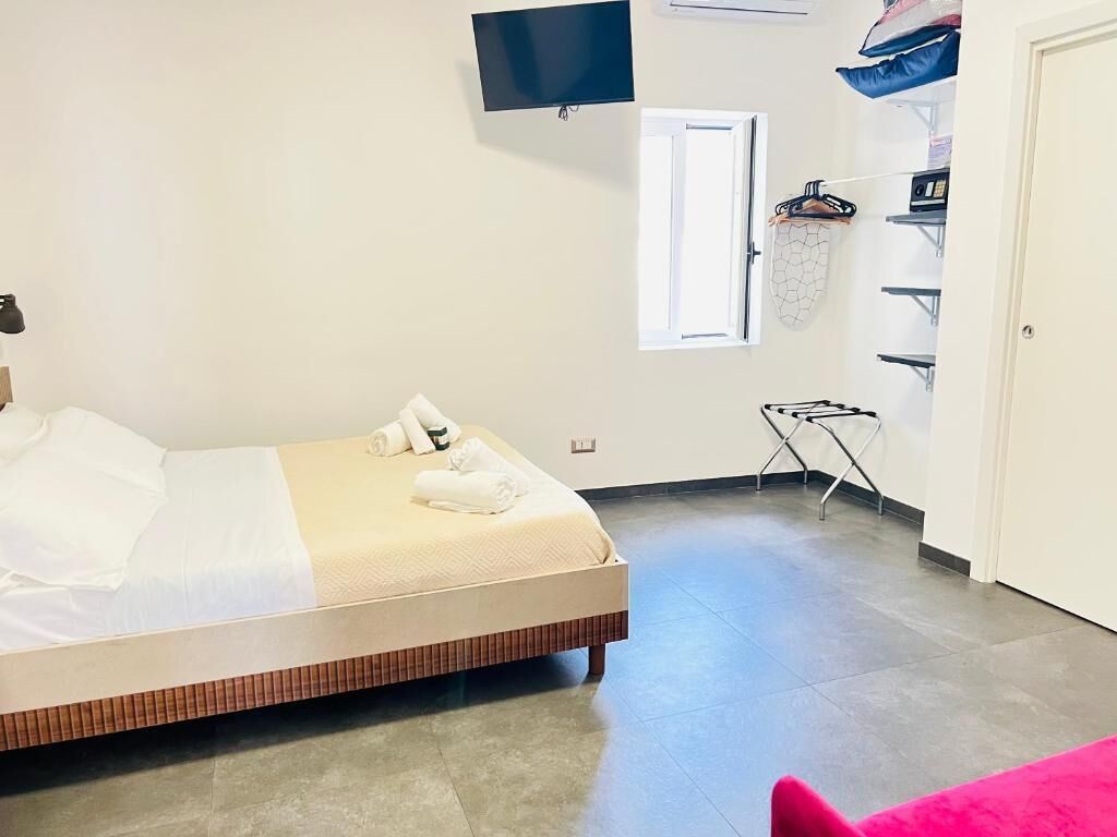 A bedroom with a bed, a TV, a window, a drying rack, and a wardrobe.