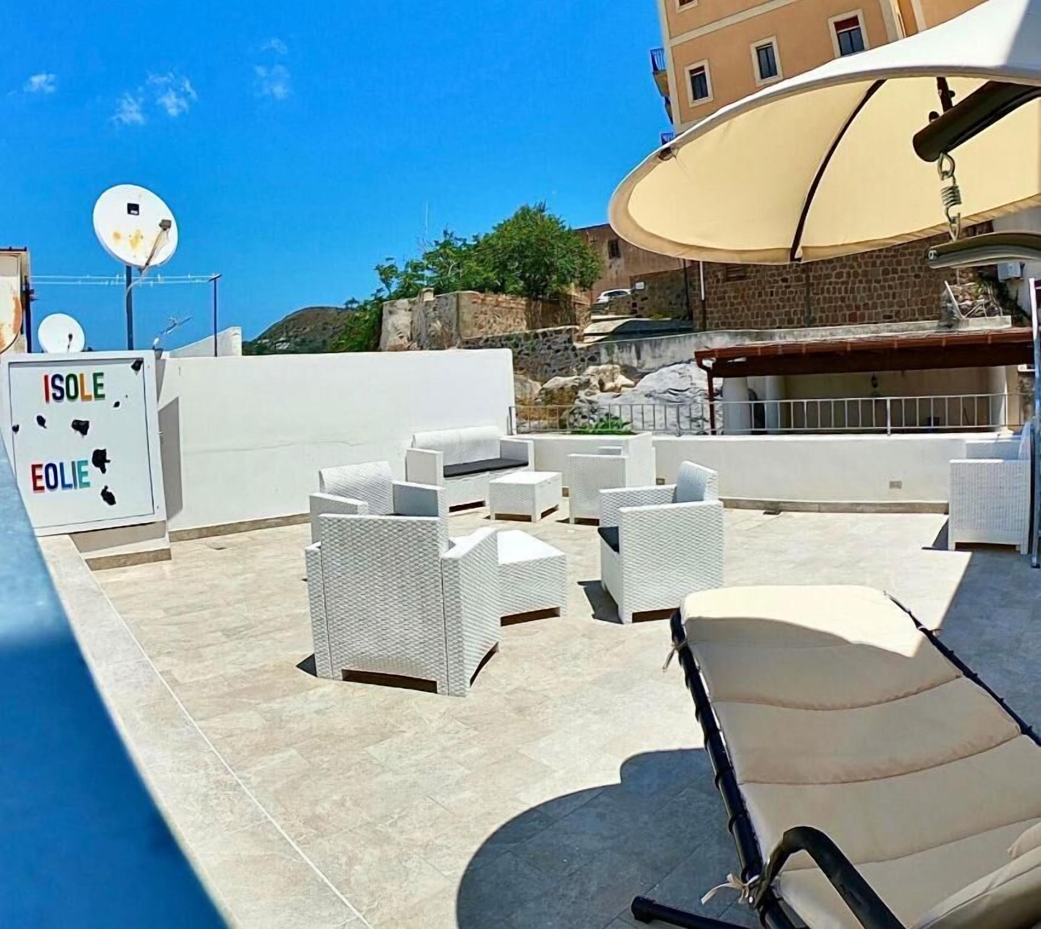 A rooftop terrace with white wicker furniture, a pool, and a large umbrella.
