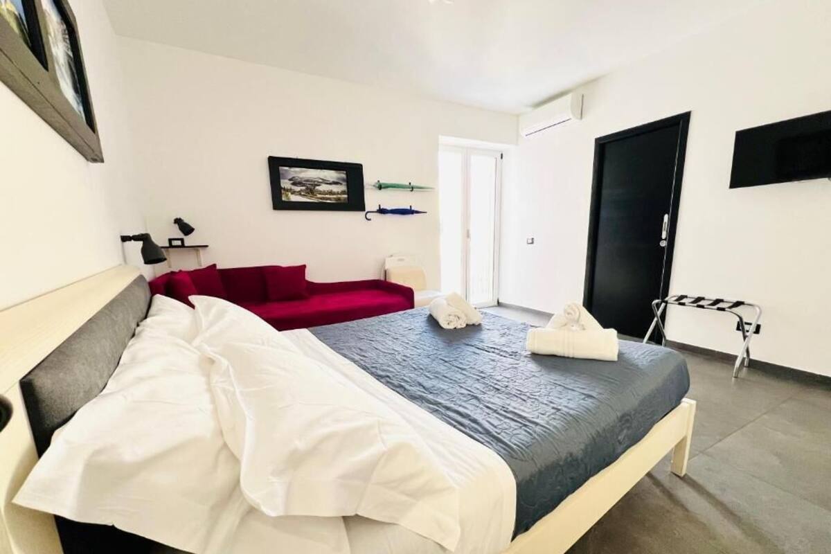 Un dormitorio con cama, un sofá rojo, un escritorio con silla, un televisor y una puerta.