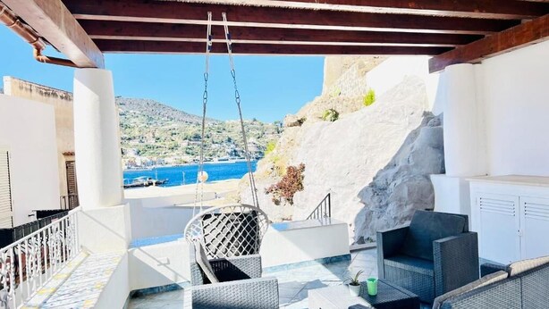 Eine Terrasse im Freien mit Korbmöbeln, Blick auf das Meer und einen felsigen Hang.