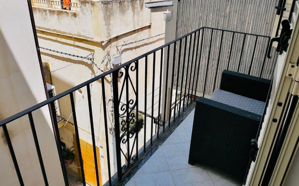 A narrow balcony with a black metal railing, a small enclosed seating area, and a view of the street below.