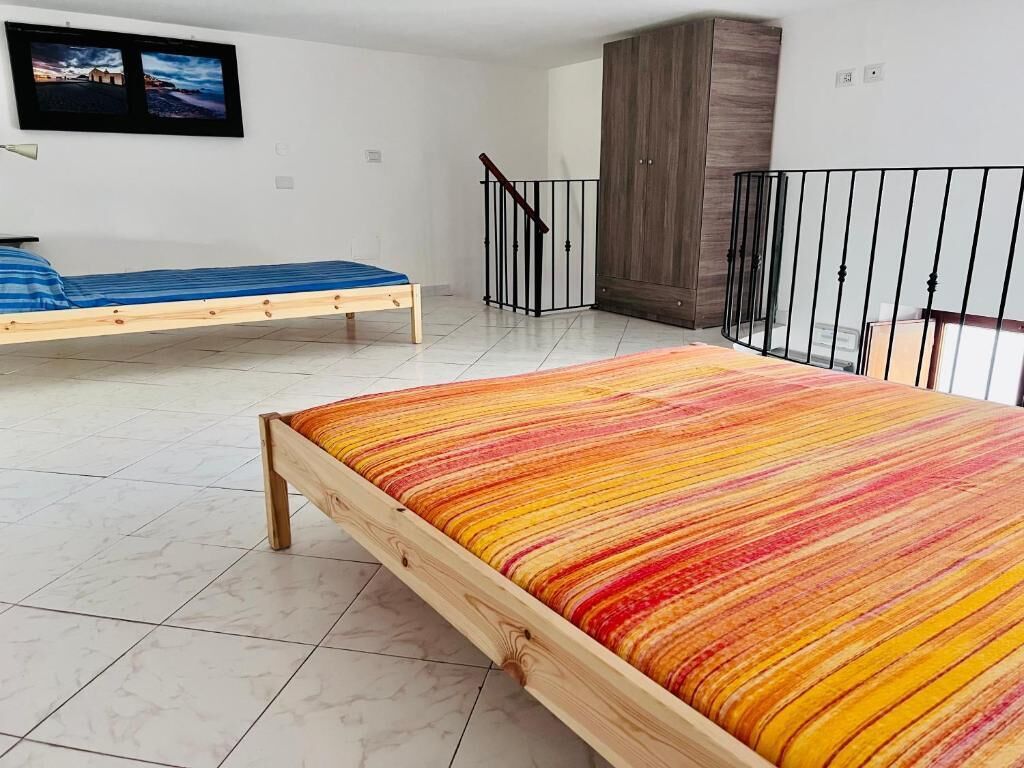 A bedroom with a wooden bed, a blue mattress, a colorful striped blanket, a wardrobe, and a balcony with a railing.