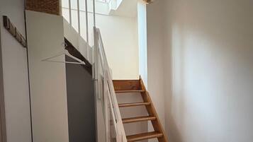 Un escalier avec des marches en bois menant à un palier, un mur blanc et un luminaire suspendu.