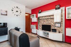 A modern living room with a stone wall, a flat-screen TV, a clock, and a red accent wall. - Apartment 'La Casa Di Kira' with Private Garden and Wi-Fi (Lucca)