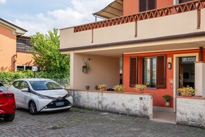 A residential building with a red door, potted plants, and a parked white car. - Apartment 'La Casa Di Kira' with Private Garden and Wi-Fi (Lucca)