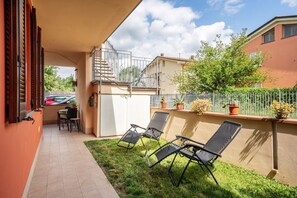 Une terrasse couverte avec deux chaises longues, une table et un escalier menant à un niveau supérieur.