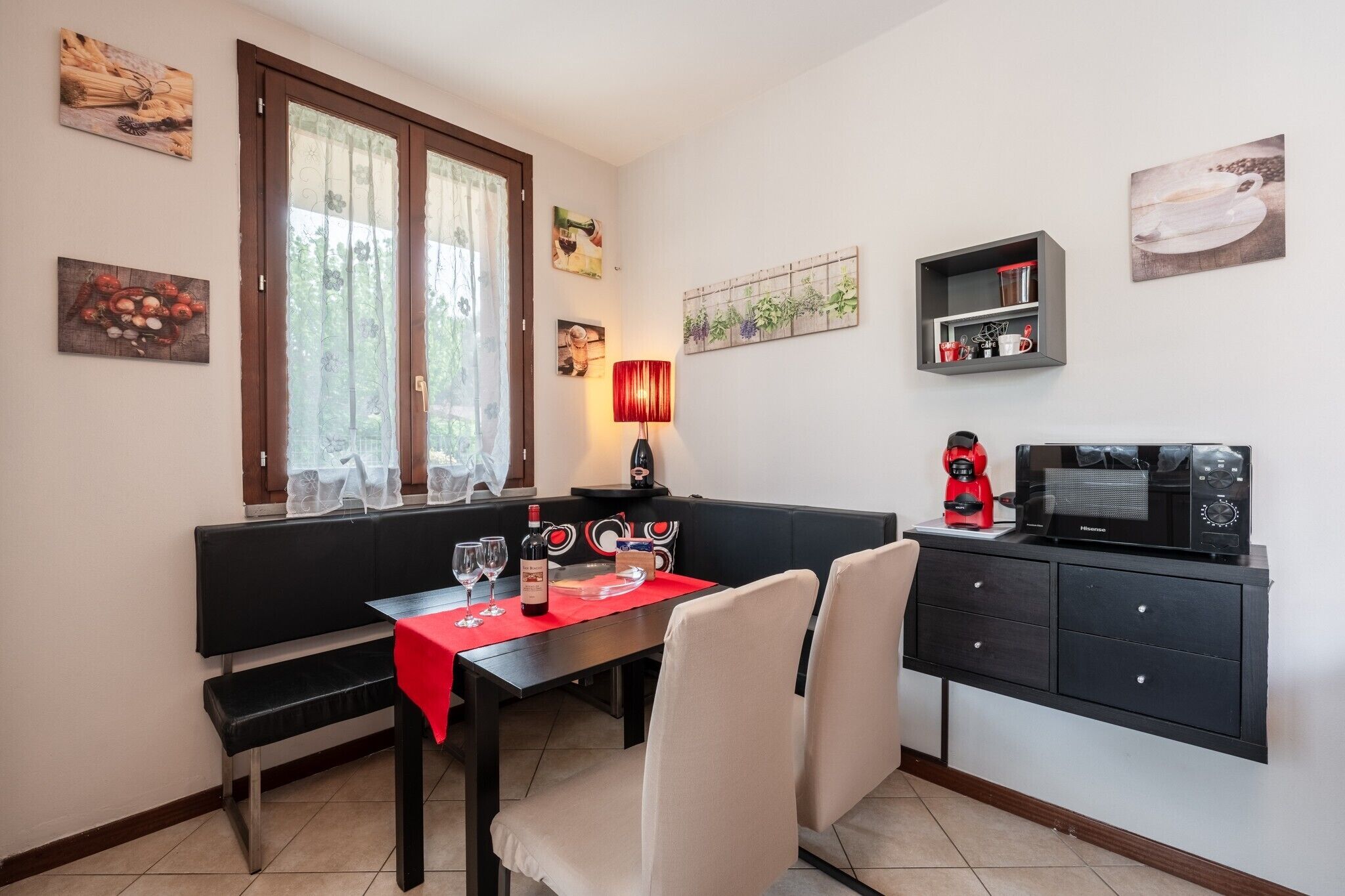 Ein Essbereich mit einem Tisch für zwei Personen, einer Bank, einer Kaffeemaschine und einer Mikrowelle auf einem schwarzen Schrank.