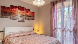 Une chambre à coucher comprenant un lit, une table de chevet, une lampe fixée au mur et une fenêtre avec des rideaux légers.
