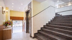 A hotel lobby with a marble staircase, a reception desk, and a flower arrangement. - Manthra Hotel Arakere Bannerghatta (Bengaluru)