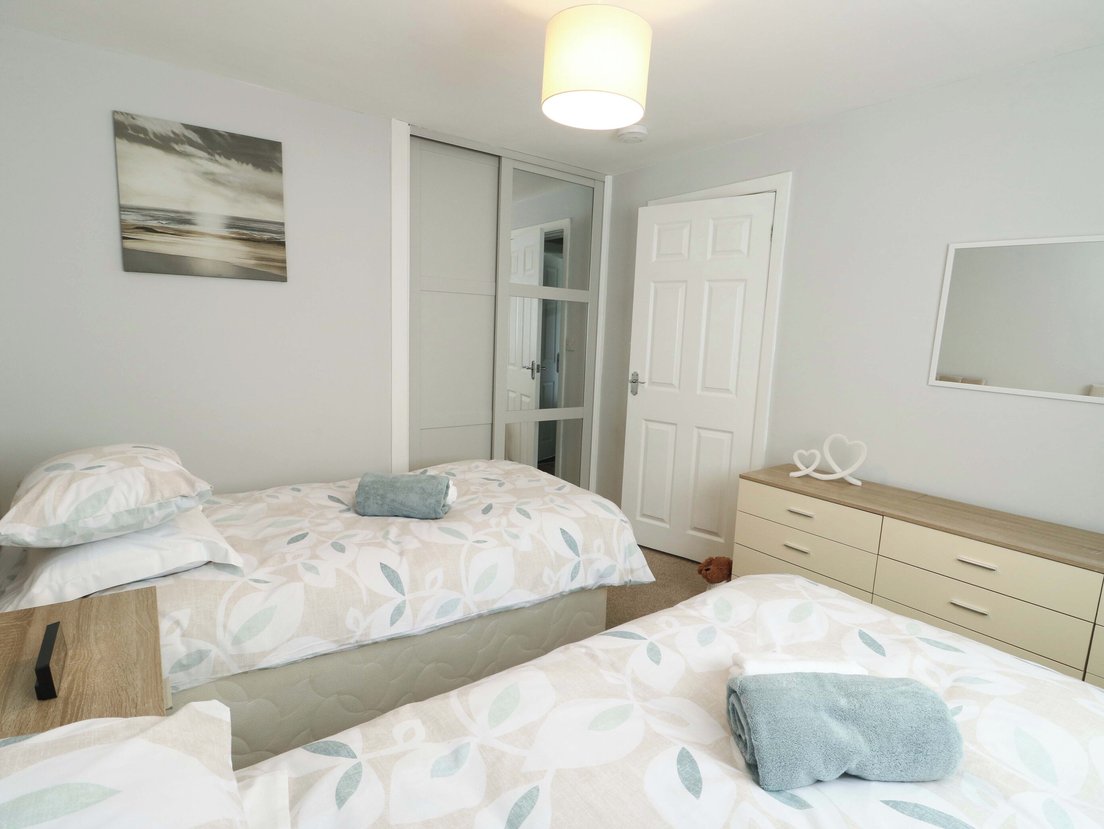 A bedroom with two beds, a wardrobe, a mirror, and a door leading to a bathroom.