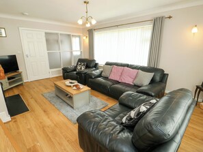 A living room with a black leather sofa, a wooden coffee table, a television, and a sliding door. - Min Y Cae (Cemaes Bay)
