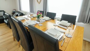 Une salle à manger avec une table en bois dressée pour six personnes, des chaises en cuir noir, un vase de fleurs et une décoration en forme de cœur accrochée au mur.