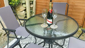 Une table ronde en verre, deux chaises, une bouteille de champagne et deux verres.