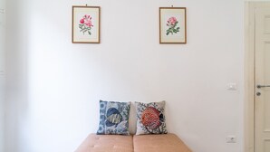 Ein Zimmer mit einem beigefarbenen Sofa, zwei gerahmten floralen Bildern an der Wand und einer Tür rechts.