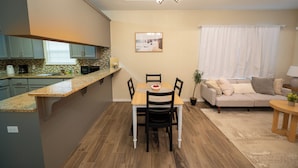 Eine moderne Küche mit Essbereich, ausgestattet mit einem Holztisch, Stühlen und Blick zum Wohnzimmer mit Sofa und Vorhängen.