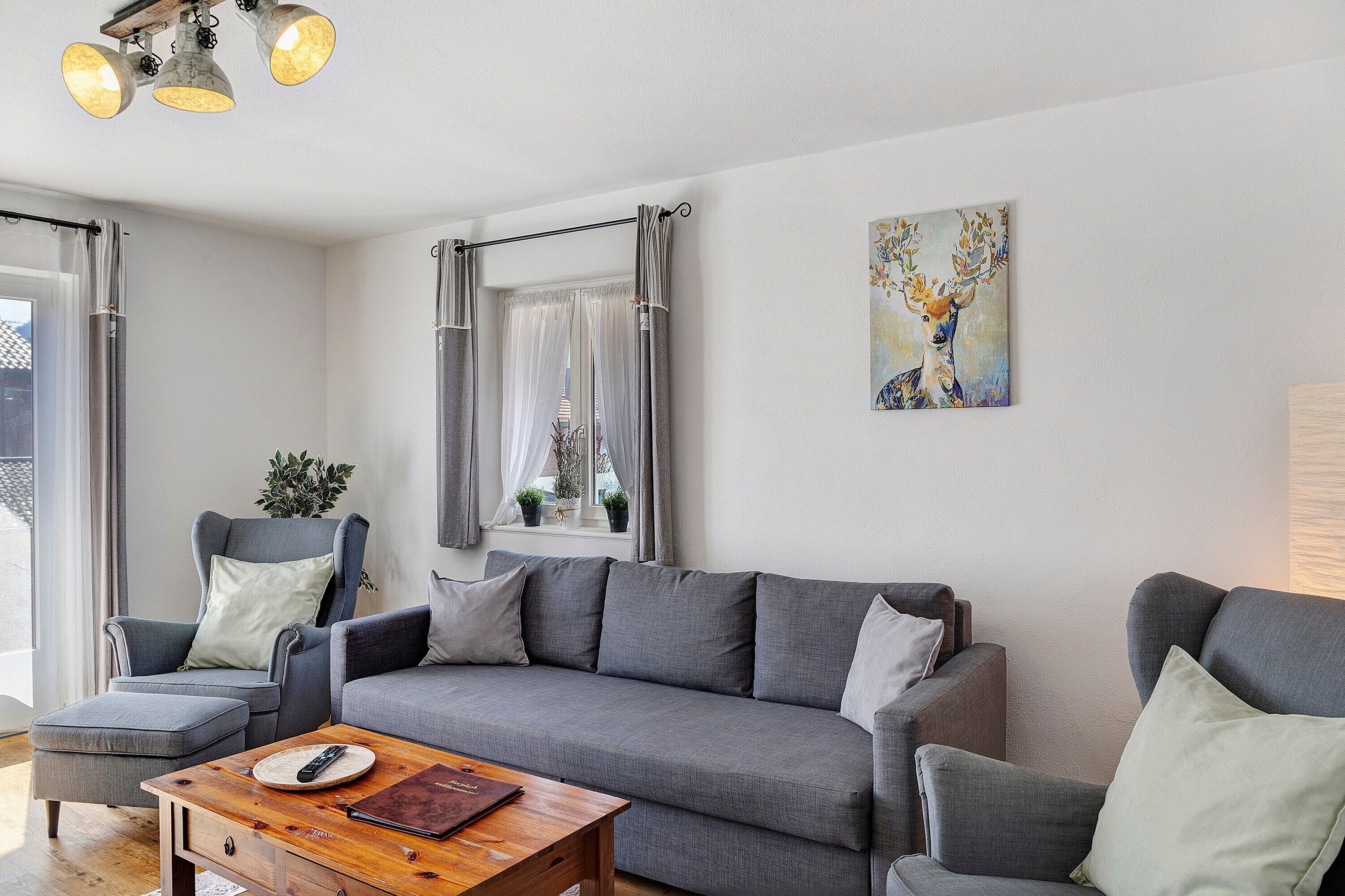 Un salon moderne avec un canapé gris, un fauteuil assorti, une table basse en bois et un tableau représentant un cerf accroché au mur.