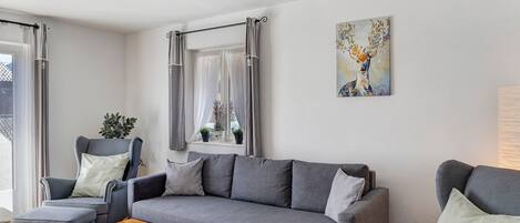 Un salon moderne avec un canapé gris, un fauteuil assorti, une table basse en bois et un tableau représentant un cerf accroché au mur.