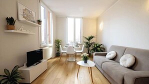 A modern living room with a sofa, TV, dining table, chairs, and potted plants. - Exclusive suite with Cathedral view | Elegant design in the heart of Ferrara (Ferrara)