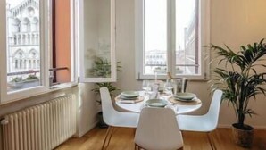 A dining area with a table set for two, large windows, and a radiator. - Exclusive suite with Cathedral view | Elegant design in the heart of Ferrara (Ferrara)