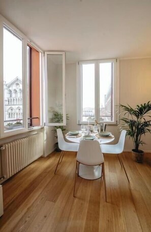A dining area with a table set for two, large windows, and a radiator. - Exclusive suite with Cathedral view | Elegant design in the heart of Ferrara (Ferrara)