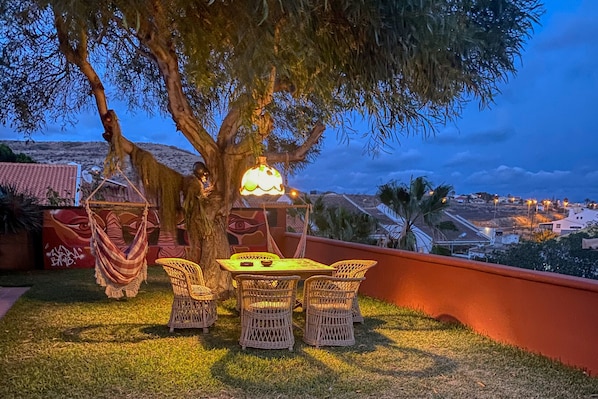 A patio with wicker furniture, a table, and a hanging light fixture. - Casa Saudade, a Home in Madeira (Porto Santo)