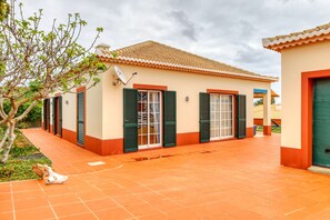 A building with a tiled roof, green shutters, and a tiled patio. - Casa Saudade, a Home in Madeira (Porto Santo)