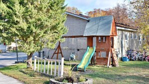 A playground with a slide and swings, a tree, and a building with a brick facade.