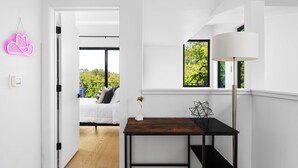A modern room with a bed, a desk with a lamp, and a view of greenery outside. - Alluring Sophistication Meets Mid-Century Chic (Austin)