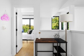 A modern room with a bed, a desk with a lamp, and a view of greenery outside. - Alluring Sophistication Meets Mid-Century Chic (Austin)