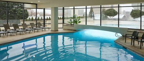 Una piscina interior con vistas despejadas al exterior a través de amplios ventanales, rodeada de sillones de descanso.