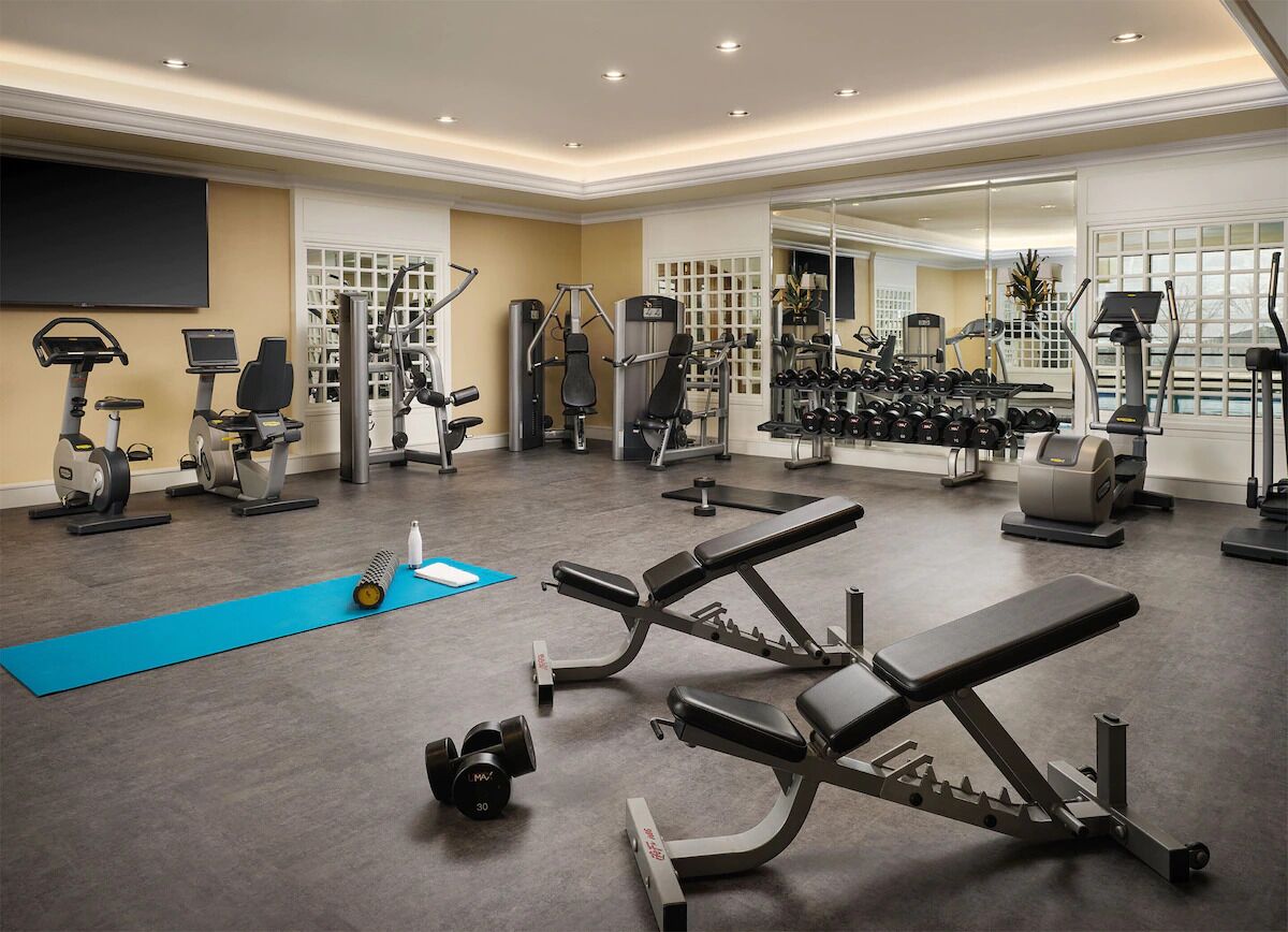 Un gimnasio bien equipado con diversas máquinas de ejercicio, pesas y una colchoneta azul en el suelo.