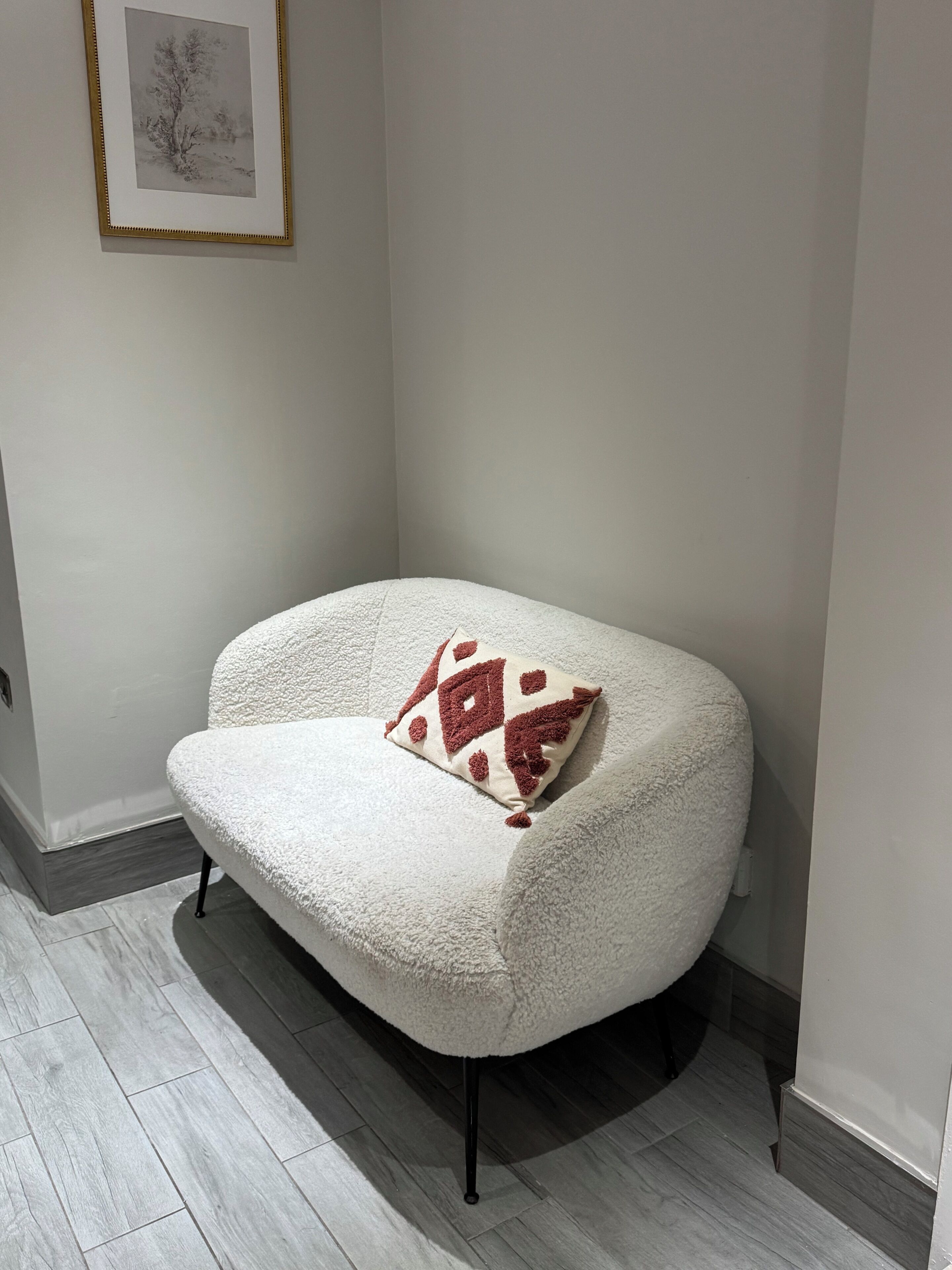 A corner sofa with a patterned cushion, a framed picture on the wall, and a wooden floor.
