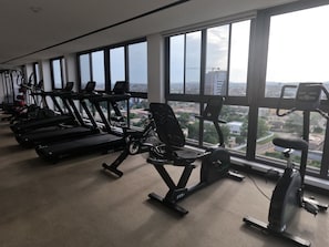 Ein Fitnessstudio mit verschiedenen Trainingsgeräten, großen Fenstern und Blick auf die Stadt.