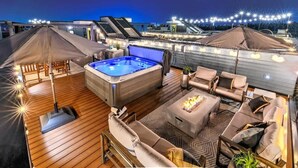 Une terrasse sur le toit avec un jacuzzi, des sièges d’extérieur et des guirlandes lumineuses.