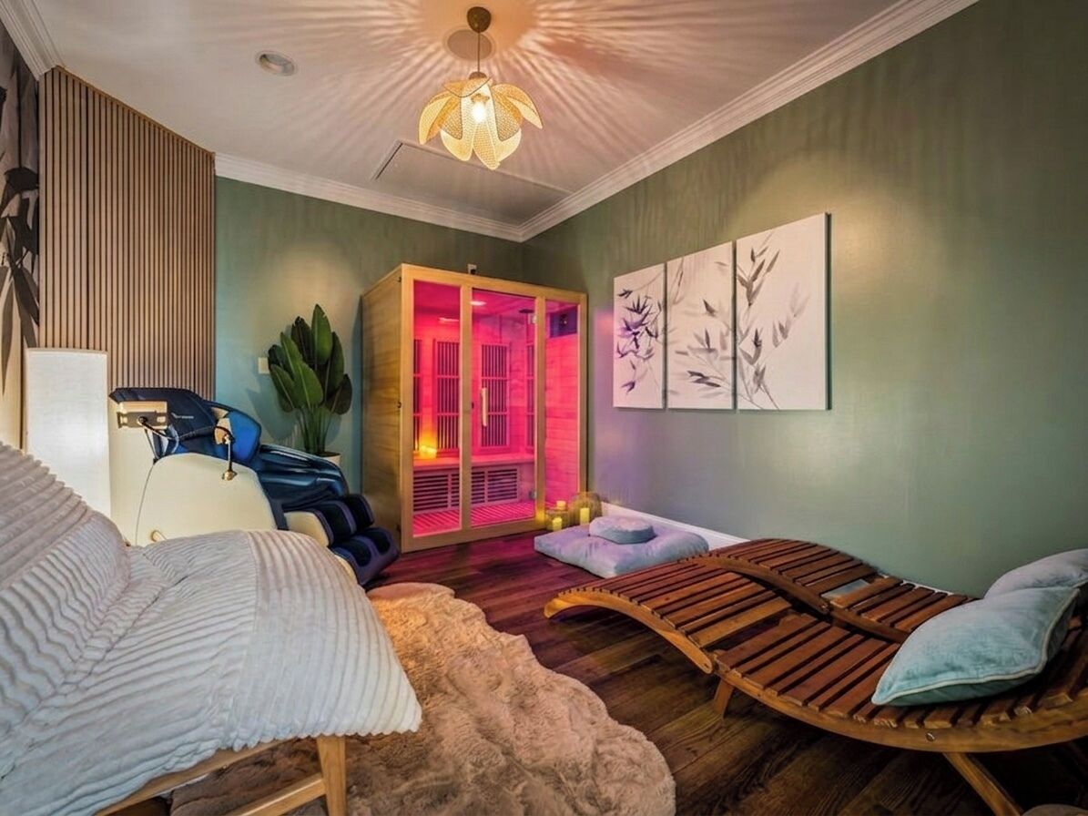 Une pièce comprenant un lit, un banc en bois, un fauteuil de massage, une table de massage et une salle de massage éclairée en rouge.