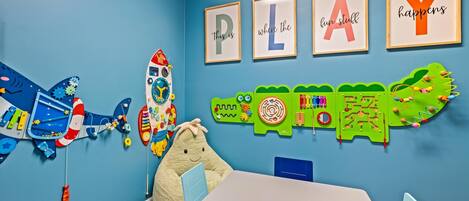 Une salle de jeux pour enfants, équipée de jouets éducatifs, d’une table, de chaises et d’affiches représentant l’alphabet, accrochées au mur.