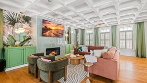 A living room with a fireplace, green cabinets, a sofa, and a painting of a sunset. - Walk 2 Beach |Theater, Games, Putt, Pool, Sleep 22 (North Myrtle Beach)