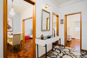 A hallway with a wooden floor, a white console table with decorative items, a mirror, and a chandelier. - Algarve Townhouse in Loulé by MGM Stays (Loulé)